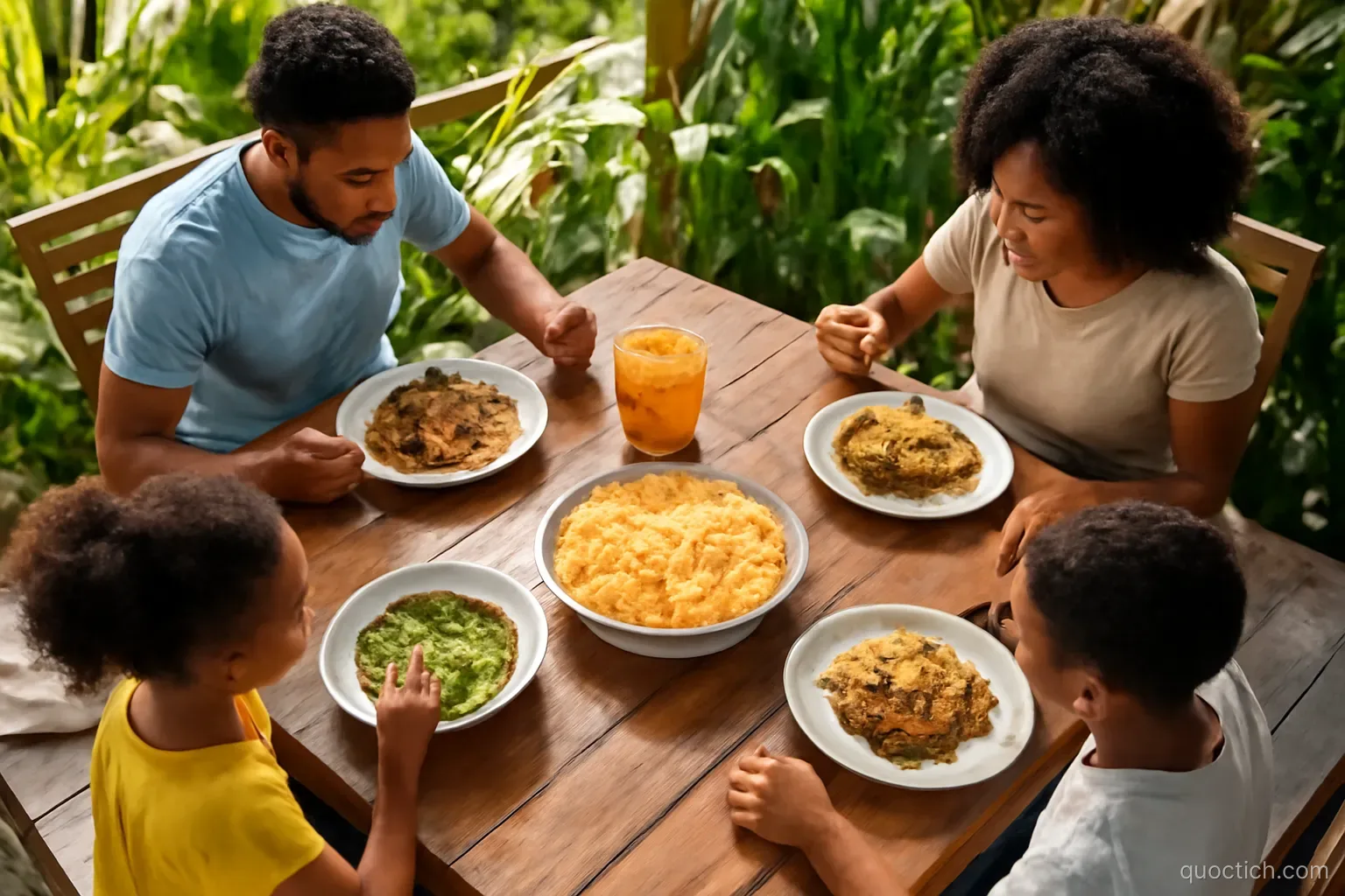 Overhead view of a family Sunday lunch on a wooden table on a sunny veranda in Grenada: green callaloo soup, golden macaroni pie, stewed chicken, rice and peas, passion fruit juice, tropical plants around
